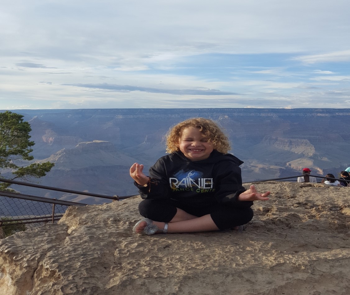 A young girl sitting cross legged meditating on a rock overlooking grand canyon