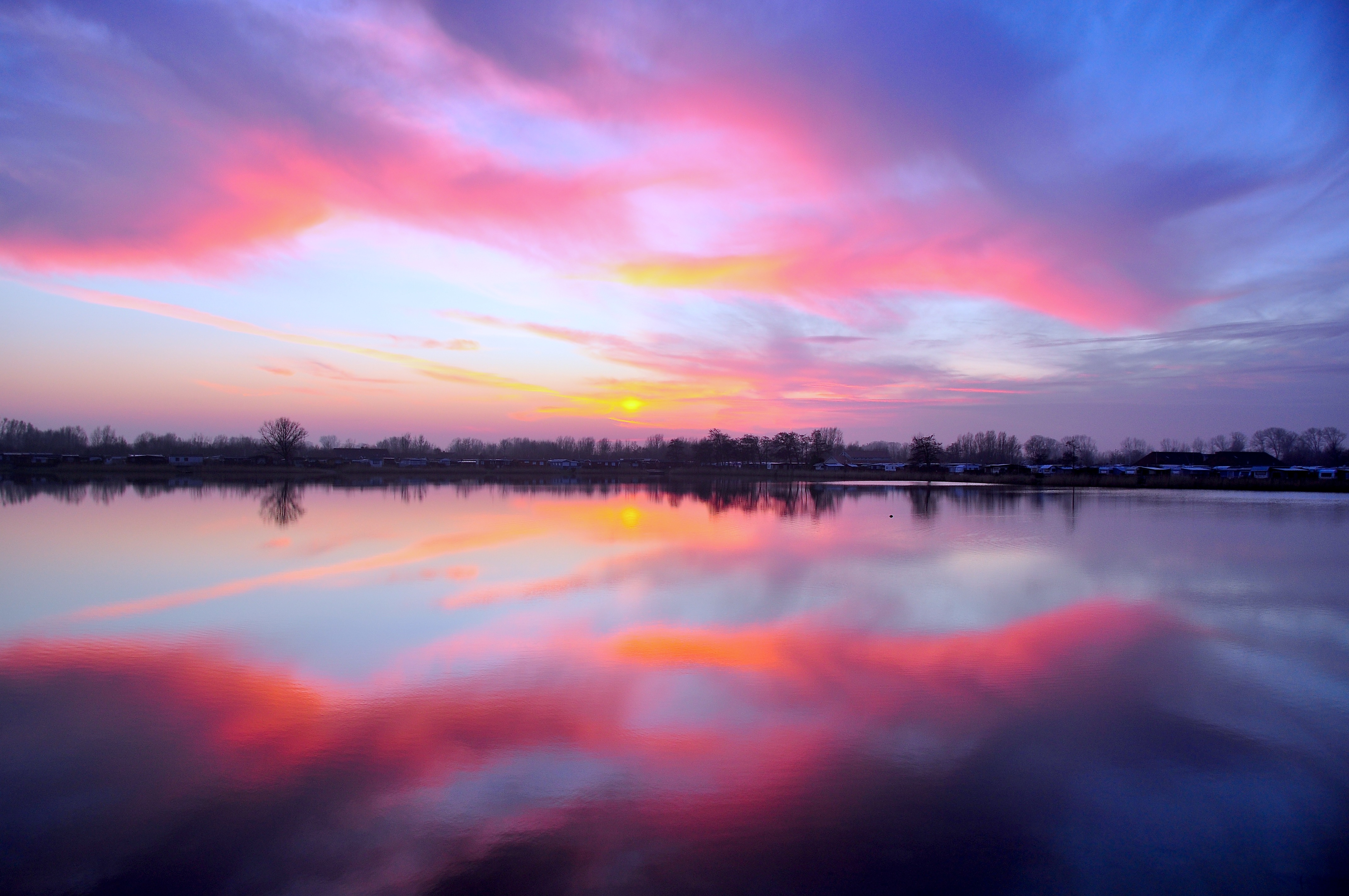 The sunset illuminating a rainbow in the clouds above still water