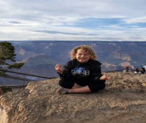 A young girl sitting cross legged meditating on a rock overlooking grand canyon