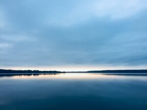 Calm lake at dusk perfectly reflecting a soft blue overcast sky, water and sky mirroring each other