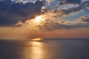 Golden sunbeams breaking through storm clouds over a calm ocean, light pushing through the heaviness