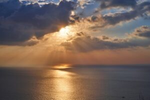 Sunbeams breaking through dramatic storm clouds over the ocean, light rays reflecting on the water below